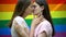 Lesbians kissing passionately on rainbow flag background, same-sex relationship
