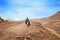 Lesotho, african young shepherd man in national wool blanket dress and balaclava cap goes along rural high mountain road, blue sky