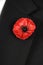 Lest We Forget Red Poppy Lapel Pin Badge on black suit - vertical.