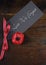 Lest We Forget, Red Poppy Lapel Pin Badge on dark recycled wood - vertical