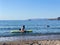 Lesvos, Greece - 29 August 2020: Attractive young woman wearing a pink bikini sitting relaxing with friend on sup board
