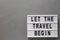 `Let the travel begin` on a lightbox on a gray surface, top view. Flat lay, from above, overhead. Copy space