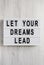 `Let your dreams lead` on a lightbox on a white wooden surface, overhead view. Flat lay, top view, from above