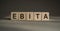 Letter block in word EBITA abbreviation of earnings before interest, taxes and amortization on gray background