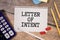 LETTER OF INTENT text on a paper clipboard with magnifier and keyboard on wooden background