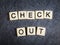 Letter tiles on black slate background spelling Check Out