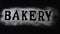 Letters of word bakery made with sieved flour on black table background, Preparation for baking, horizontal banner, Lettering