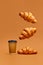Levitating food. Crispy fresh croissants flying over coffee cup to go on brown background.