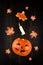 Levitating halloween pumpkin Jack lantern and burning candle against dark wooden surface, autumn maple leaves around