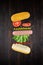 Levitating hot dog ingredients: sausage, mustard, ketchup, lettuce, tomatoes and bun on brown wooden plank surface