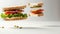 Levitating sandwich layers with vegetables, meat, and cheese. Grey background