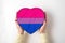 LGBT bisexual pride flag on a heart shape box in female hands. Pride symbol. Top view