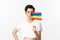 Lgbtq community. Attractive queer man with flitter on face, waving pride rainbow flag and looking at camera, standing in