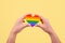 LGBTQ rights concept, Rainbow heart shape in female hand on yellow background