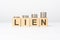 lien text written on wooden block with stacked coins on white background, growing trend