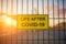 Life After COVID-19 sign on a fence with blured city view on a background at sunset