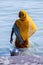 Life on the Ganges: woman in a bright yellow or orange sari with a metal bucket bathing in the Ganges as religious ritual.