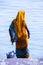 Life on the Ganges: woman in a bright yellow or orange sari with a metal bucket bathing in the Ganges as religious ritual.