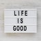 `Life is good` words on a lightbox on a white wooden background, top view. Overhead, from above, flat lay