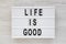 `Life is good` words on a lightbox on a white wooden surface, top view. Overhead, from above, flat lay. Close-up