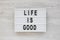 `Life is good` words on a modern board on a white wooden surface, top view. Overhead, from above, flat lay