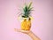 When life hands you pineapples make pina coladas. a woman holding a pineapple with glasses on against a pink background.