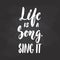 Life is a song. Sing it - hand drawn Musical lettering phrase isolated on the black chalkboard background. Fun brush