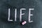 Life. A word written in pink chalk on a black chalkboard. Handwritten text. A piece of colored chalk hangs next to it