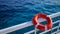 lifebuoy attached to a ship\\\'s white railing, with the clear blue sea in the background