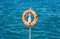 Lifebuoy orange on vertical iron against blue sea background