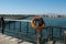 Lifebuoy and pier. Orange lifebuoy on barrier pillar. Save lifebuoy and blue water. Safety equipment on dock for emergency.