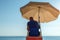 A lifeguard on the beach sits in a chair under a sun umbrella