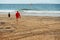 Lifeguard dressed in red walking to the ocean and a small boy boy with small surf board