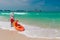 Lifeguard on duty seen from behind with orange boat and paddle in hand.