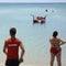 Lifeguard man watching the sea with turquoise water. Beside him a fat woman is phoning