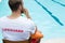 Lifeguard sitting on chair and blowing whistle at poolside