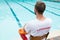 Lifeguard sitting on chair with rescue buoy at poolside