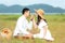 Lifestyle couple happy honeymoon in sunny time. Asian young couple sitting picnic and relax in the meadow and field near river and