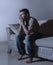 Lifestyle dramatic light portrait of young sad and depressed man sitting at shady home couch in pain and depression feeling stress