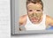 Lifestyle funny portrait of young attractive and surprised man horrified looking himself on bathroom mirror ugly and weird face ap