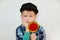 Lifestyle and people concept. Adorable little boy in cap and checked shirt with blue eyes holding lollipop in his one hand and hol