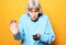 Lifestyle and people concept: funny grandma is holding a TV remote over yellow background