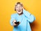 Lifestyle and people concept: funny grandma is holding a TV remote over yellow background