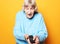 Lifestyle and people concept: funny grandma is holding a TV remote over yellow background