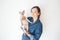 Lifestyle photo of a casual dressed female in blue jeans shirt holding and cuddling cute and funny Devon Rex cat. Happy kitty in