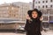 Lifestyle portrait of beautiful brunette model with bright makeup in fashionable coat and hat posing at the city street