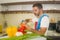 Lifestyle portrait of young handsome and happy man in red apron cutting carrot preparing vegetables salad smiling cheerful in home