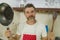 Lifestyle portrait of young handsome and happy man in red apron holding cooking pan and wooden spoon smiling cheerful in home cook