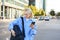 Lifestyle shot of young woman, student standing with smartphone on the street, opening her backpack pocket