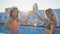 Lifestyle, young girls in swimsuits show heart sign with hands on background of sun rays at summer resort